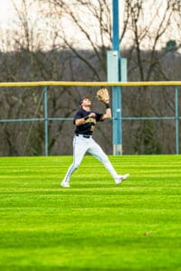 Baseball player preparing to catch a fly ball on a sunny day in the outfield, showcasing athleticism and focus.