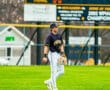 High school baseball player walking on the field, scoreboard showing 21 at-bat, 2 balls, 2 strikes, game in session.