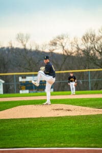 High school baseball pitcher in a black jersey stands on the mound, ready to deliver a pitch during a game.