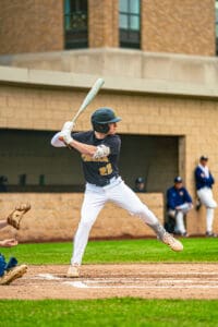High school baseball player in a batting stance, preparing to hit during a game on a sunny day.