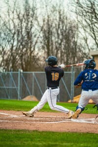 Baseball player in action, swinging a bat at home plate during a game, with an opponent catching nearby.