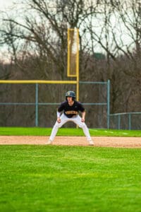 Baseball player in a crouched position on the field, focused and ready for the next play in a sunny afternoon game.