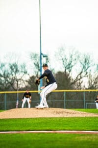 A young baseball pitcher winds up on the mound during a game; teammates position themselves in the background.