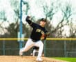 A baseball pitcher in a black jersey winds up on the mound during a game, showcasing athletic form and intensity.