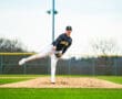 Young baseball player pitching from the mound on a grassy field, wearing a team uniform and focused on the game.
