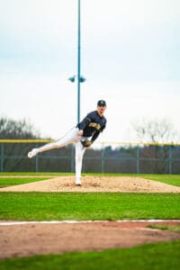 Young baseball player pitching from the mound on a grassy field, wearing a team uniform and focused on the game.