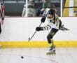 Young athlete skating and shooting a puck in a roller hockey game, with a referee in the background for officiating.