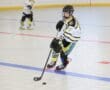 Young hockey player skating with a stick and puck on a roller hockey rink, showcasing athletic skill and strategy.
