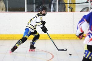 Youth roller hockey player in action, skillfully skating and controlling the puck on a rink.