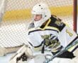 Youth ice hockey goalie in action, wearing a white and black jersey, focused on the game in a rink setting.