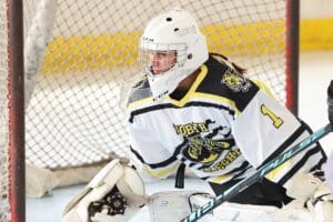Youth ice hockey goalie in action, wearing a white and black jersey, focused on the game in a rink setting.