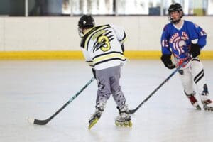 Two young players compete in roller hockey on an indoor rink, showcasing skill and teamwork in their game.