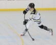 Young hockey player in action, skating on a rink while handling a stick, wearing a white and black jersey.