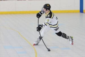 Young hockey player in action, skating on a rink while handling a stick, wearing a white and black jersey.