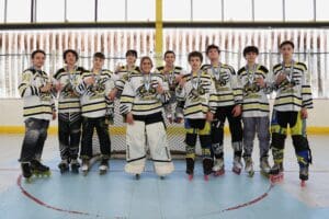 Youth roller hockey team celebrating with medals in front of a goal, showcasing camaraderie and athletic achievement.