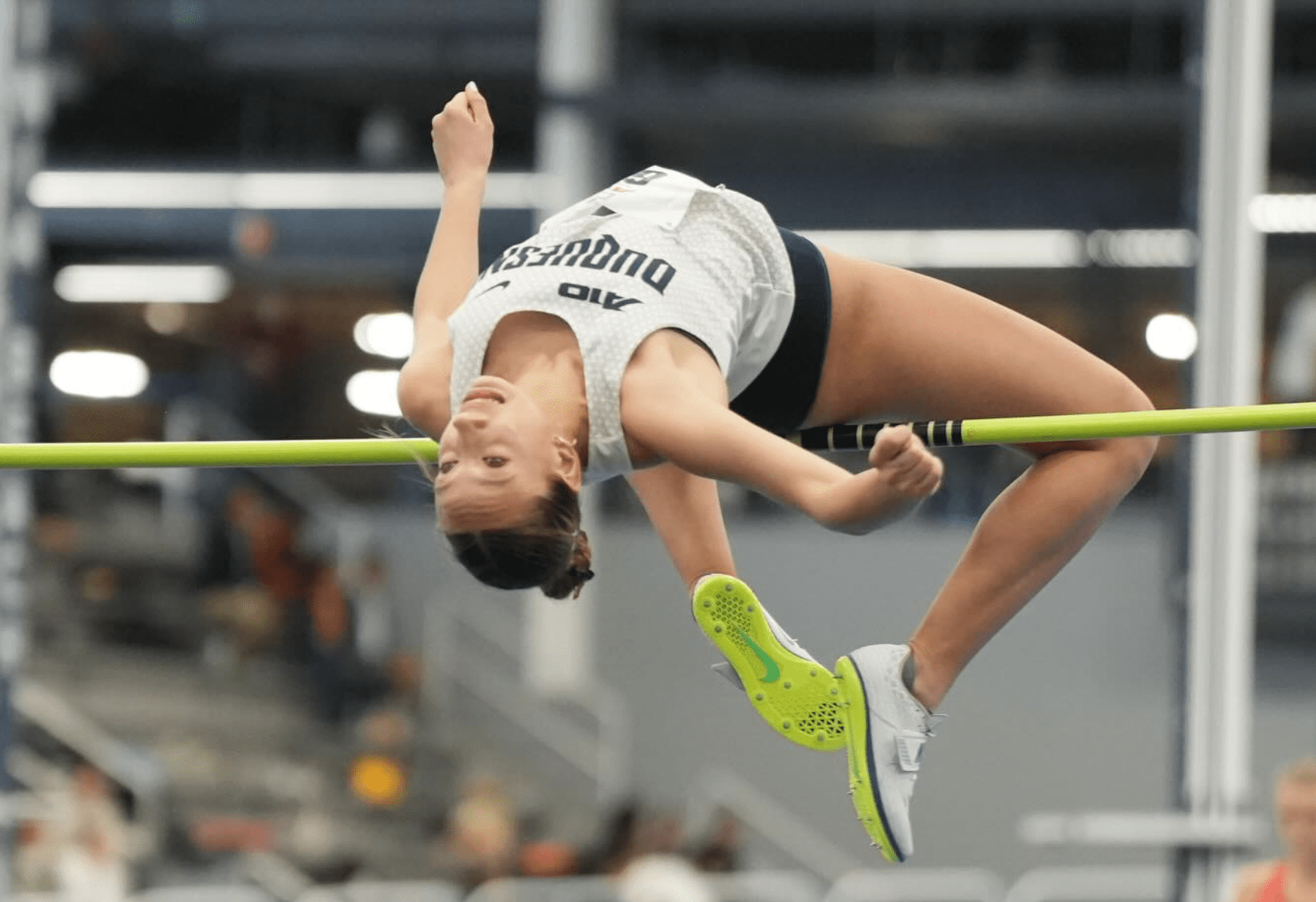 Female high jumper clears the bar in a competitive track and field event, showcasing athleticism and skill.