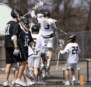 Lacrosse players celebrate a goal, showcasing teamwork and excitement on the field during a sunny game day.