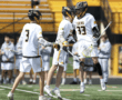 High school lacrosse players celebrate a goal, showcasing teamwork and excitement on a sunny day in a stadium.