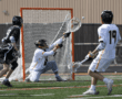 Lacrosse players in action, featuring a goalie making a save during a game on a sunny field.