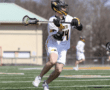 Lacrosse player in action, preparing to make a powerful shot on a sunny field. Team colors: white and yellow.