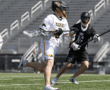 Lacrosse players in action on the field, one in white and one in black, showcasing athletic intensity during a game.