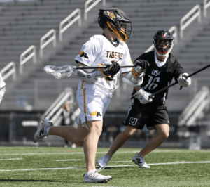 Lacrosse players in action on the field, one in white and one in black, showcasing athletic intensity during a game.