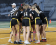 A group of female players in black jerseys huddle on a football field, preparing for their flag football game.