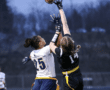 Two female athletes compete for a football in a dynamic moment during a flag football game under dim lights.