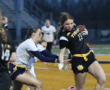 High school girls' flag football game, player in black uniform dodges a defender while carrying the ball. Action shot.
