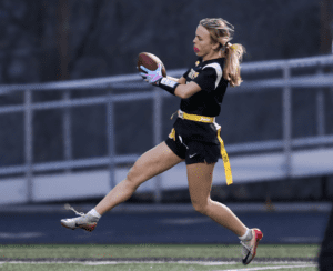 Female athlete catching a football during a flag football game, showcasing agility on the field at dusk.