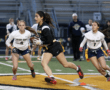 Girls' flag football game: an athlete runs with the ball as teammates chase on the field during a competitive match.