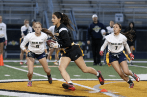 Girls' flag football game: an athlete runs with the ball as teammates chase on the field during a competitive match.