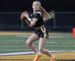 A young female football player prepares to throw a pass on a field during a night game, showcasing athletic skill and focus.