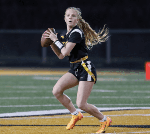 A young female football player prepares to throw a pass on a field during a night game, showcasing athletic skill and focus.