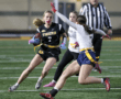 Female athlete in a black jersey running with a football, dodging defenders on a field during a flag football game.