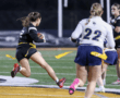 Female player runs with a football during a night flag football game on the field, showcasing athletic action and teamwork.