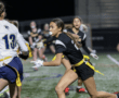 Flag football players sprint on a field during a night game, showcasing teamwork and athleticism.