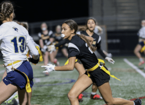 Flag football players sprint on a field during a night game, showcasing teamwork and athleticism.