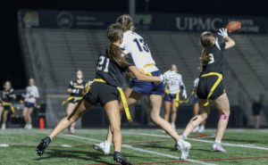 Two female players compete for a pass during a night flag football game, showcasing athleticism and teamwork.