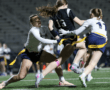 Action-packed scene of female athletes playing flag football, showcasing teamwork and competitive spirit on a well-lit field.
