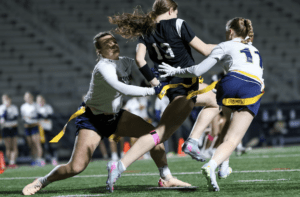 Action-packed scene of female athletes playing flag football, showcasing teamwork and competitive spirit on a well-lit field.