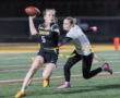 Young female athlete in action, throwing a football while being pursued in a flag football game on a field.