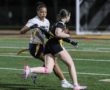Two players in a flag football game, one attempting to tag the other while running on a well-lit field.