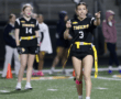 Girls flag football game: a player in a black uniform and yellow belt gestures and communicates strategies on the field.