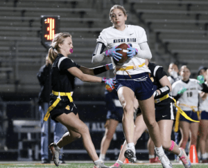 Female flag football players compete during a night game, showcasing athletic skill and teamwork on the field.