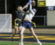 Two female athletes compete for a football in a night flag football game, showcasing skill and determination.