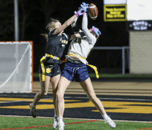 Two female athletes compete for a football in a night flag football game, showcasing skill and determination.
