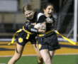 Two young female athletes celebrate a play during a night flag football game, showcasing teamwork and joy.