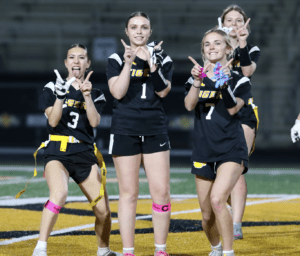 Cheerful female flag football players celebrating together on the field, showing team spirit with fun poses.