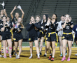Cheering girls' flag football team celebrating and posing for the camera under stadium lights, showcasing team spirit.